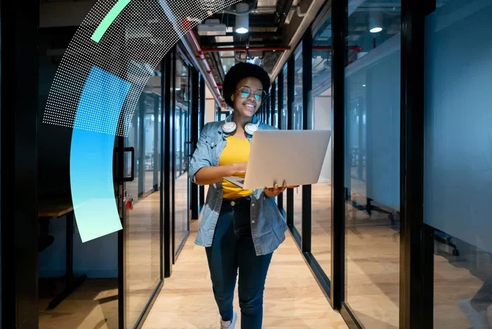 Professional walking through office hallway using laptop device.