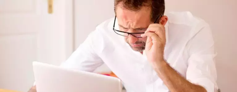 Confused man lowering his glasses while looking at his computer