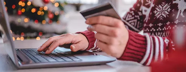 Person in a holiday sweater entering their credit card information on a laptop