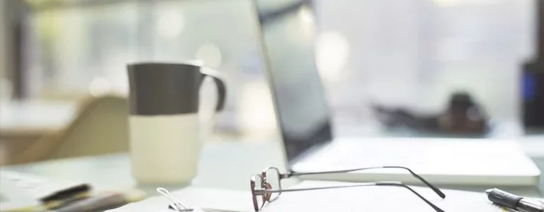 Laptop, coffee cup, and glasses on a desk