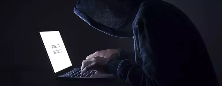 Hooded man typing on a laptop in the dark