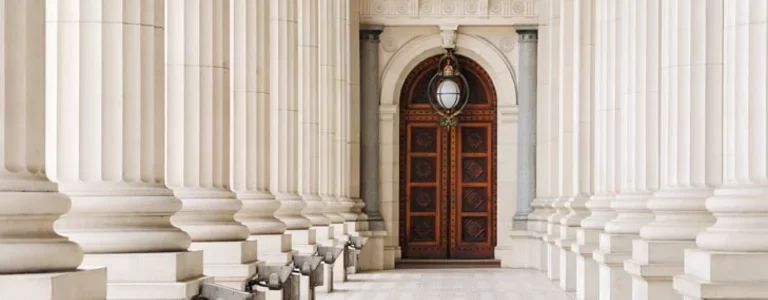 Hallway flanked by neoclassical columns leading to a wooden door