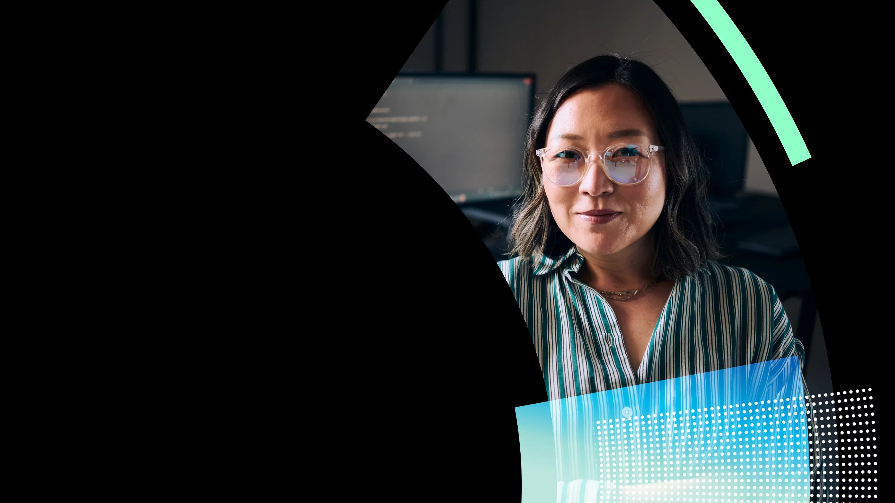 A woman with shoulder-length hair, wearing glasses and a striped blouse, poses confidently in an office setting with computer screens in the background using Proofpoint Human Risk Explorer. Soft lighting adds a warm tone to the scene.