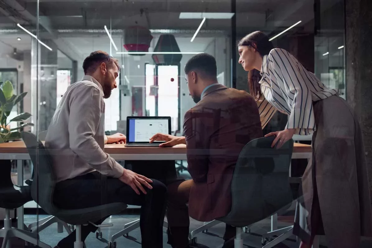 Three professionals reviewing analytics together on laptop screen.